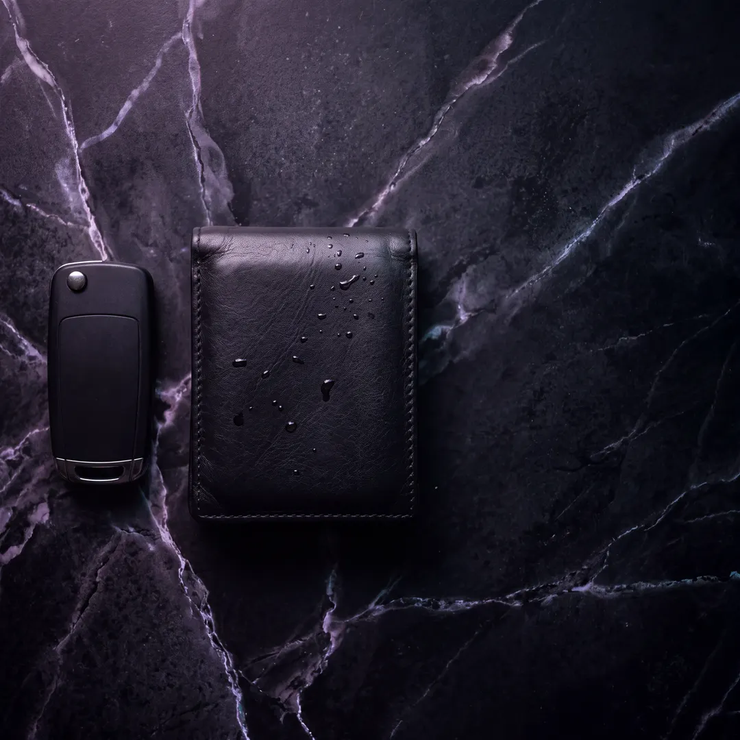 A plain car key and a leather wallet on dark marble